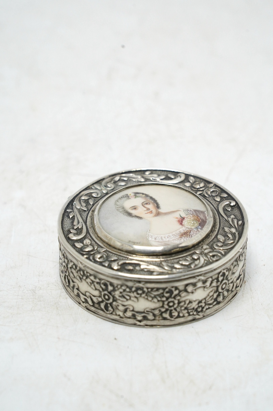 An early 20th century continental white metal circular snuff box, the cover with inset miniature watercolour of a lady signed Drepize?, 58mm. Condition - fair to good